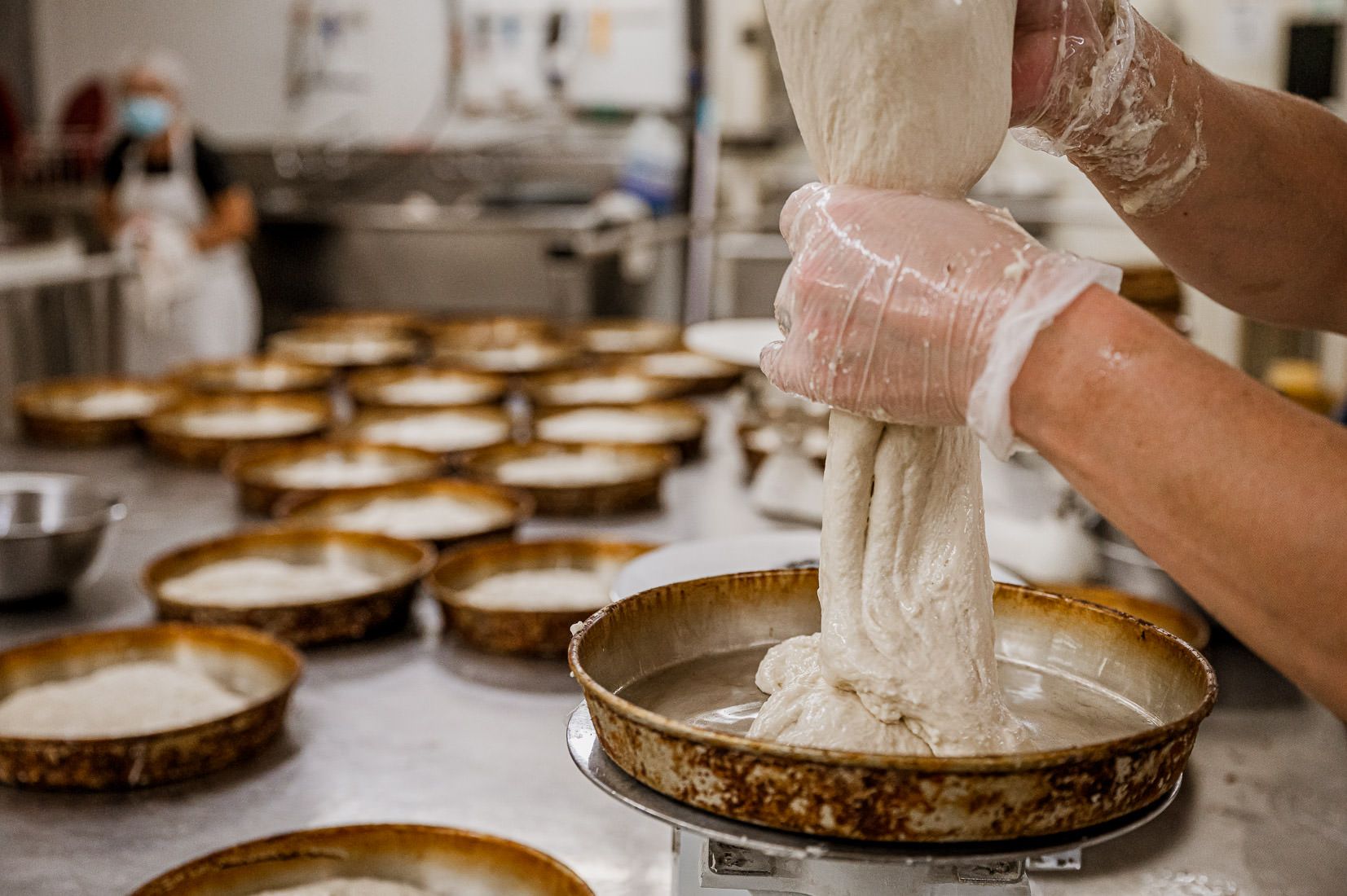 A baker portioning dough into proofing pans
